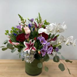 Mixed bouquet in a green glass vase with white orchids, lilies, and purple blooms