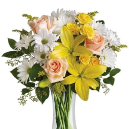 Bouquet of yellow lilies, peach roses, and white daisies in a glass vase