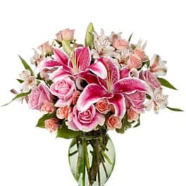 Pink lilies and roses arranged in a clear glass vase