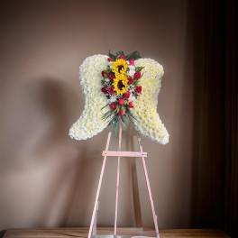 Heart-shaped floral standing spray with white flowers, red roses, and sunflowers on an easel
