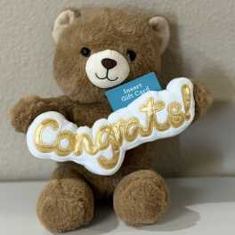 Brown teddy bear holding a "Congrats!" sign and gift card