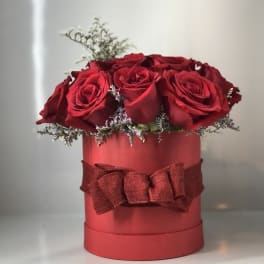 Red roses arranged in a round red box with a ribbon bow