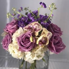 Purple roses and orchids arranged in a clear glass vase