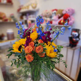 Bouquet of sunflowers, orange roses, and blue delphinium in a glass vase