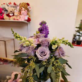 Lavender roses and purple flowers arranged in a glass vase