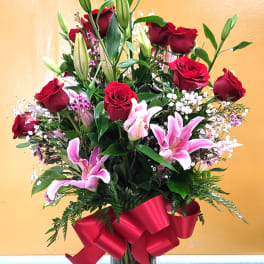 Red roses and pink lilies in a clear glass vase with a red ribbon