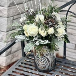 White roses in a glass vase with pinecones and winter greenery