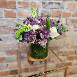 Purple and white bouquet in a glass vase on a wooden base