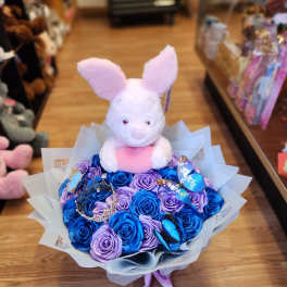 Plush bunny sitting on a bouquet of blue and lavender roses with butterfly decorations
