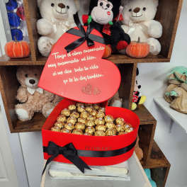Heart-shaped red gift box filled with gold-wrapped chocolates and a Spanish message.