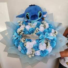 Blue plush toy atop a bouquet of blue and white roses