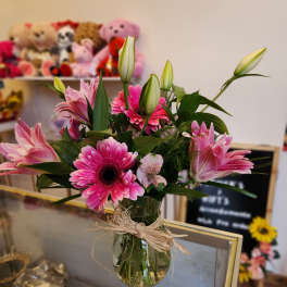 Pink gerbera daisies and lilies in a glass vase with raffia tie