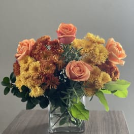 Peach roses and yellow chrysanthemums in a square glass vase