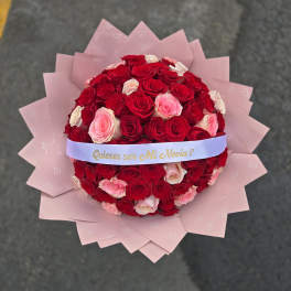 Round bouquet of red and pink roses wrapped in pink paper with a ribbon