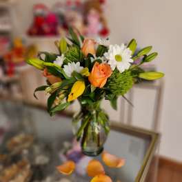 Bouquet of orange roses, white daisies, and yellow lilies in a glass vase
