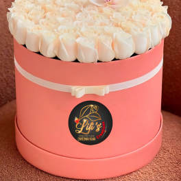 Round pink hatbox filled with white roses and a white orchid