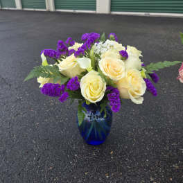 Bouquet of pale yellow roses and purple filler flowers in a blue glass vase