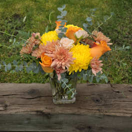 Bouquet of orange, yellow, and blush flowers in a clear glass vase