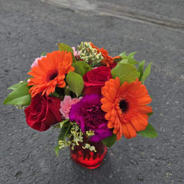 Bouquet of orange gerbera daisies and red roses in a red glass vase