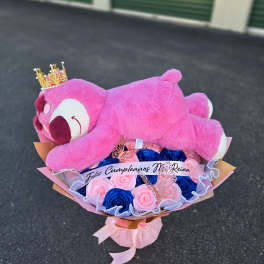 Pink teddy bear resting on a bouquet of pink and blue roses
