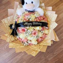Bouquet of pink and cream roses with a plush cow topper