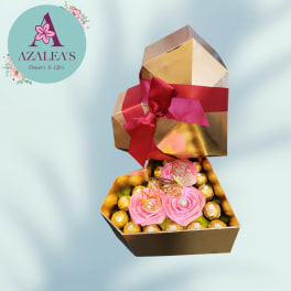 Pink rose decorations in a gold gift box with chocolates and a red ribbon