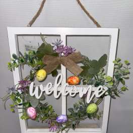 Decorative wreath in a white window frame with flowers, eggs, and a welcome sign
