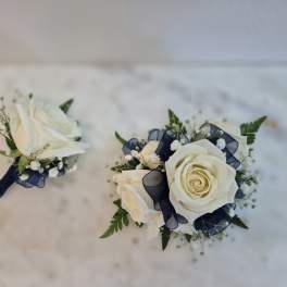 Two white rose boutonnieres with navy ribbon accents