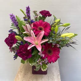 Bouquet of pink lilies, magenta gerberas, and purple carnations in a square vase