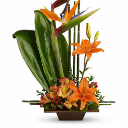 Orange lilies and bird-of-paradise in a low rectangular vase