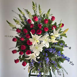 Standing floral spray with red roses, white lilies, and blue flowers
