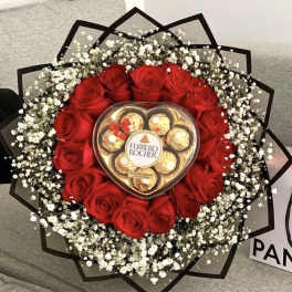 Round bouquet of red roses and white filler flowers with a heart box of chocolates in the center