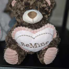 Brown teddy bear holding a heart that says "BeMine"