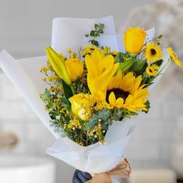 Yellow bouquet with roses, lilies, and sunflowers wrapped in white paper