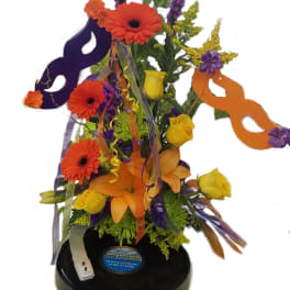 Bright mixed flower arrangement with masks and ribbons on a black base