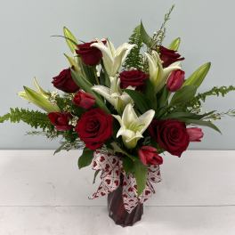 Red roses and white lilies in a glass vase with a heart-patterned ribbon
