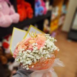 Handheld bouquet of peach roses and white baby's breath wrapped in orange mesh
