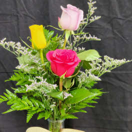 Three roses in a clear glass vase with a beige bow