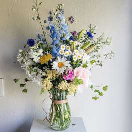 Tall mixed bouquet in a clear glass vase with blue, white, and pink flowers