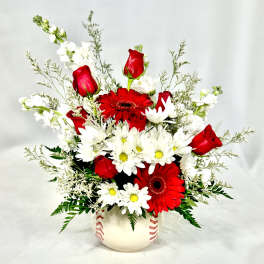 Red roses, red gerbera daisies, and white daisies arranged in a baseball-themed ceramic vase
