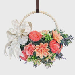 Hanging hoop wreath with peach and coral flowers and a cream checked bow