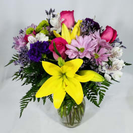 Mixed bouquet of yellow lilies, pink roses, and assorted blooms in a clear glass vase