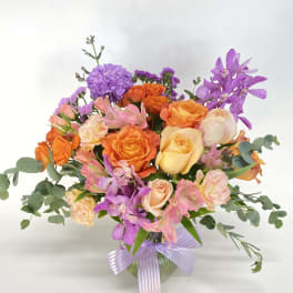 Mixed bouquet of orange, pink, and purple flowers in a glass vase