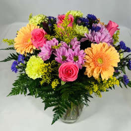 Mixed bouquet of pink, purple, yellow, and orange flowers in a glass vase