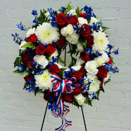 Red, white, and blue floral wreath on a stand with ribbon