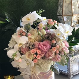 Large pastel arrangement of white orchids and mixed roses in a pink hat box with draped pearls