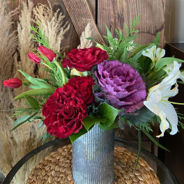 Tall corrugated metal vase with red roses, red tulips, purple ornamental cabbage, and white lilies.