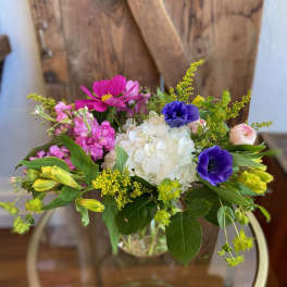 Colorful mixed bouquet with white hydrangea, purple anemones, and pink blooms in a clear glass vase