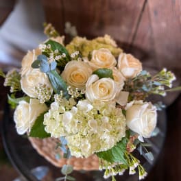 Ivory roses and white hydrangeas arranged in a basket on a glass table
