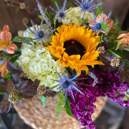 Bright mixed arrangement with sunflower, white hydrangea, purple blooms, and blue thistle-like flowers
